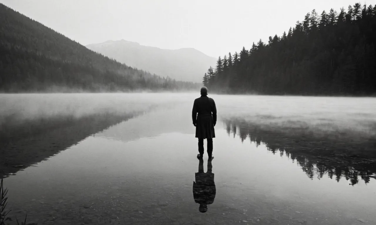 A black and white image captures a solitary figure standing at the edge of a mist-covered lake, symbolizing the mysterious journey of the soul beyond earthly existence.